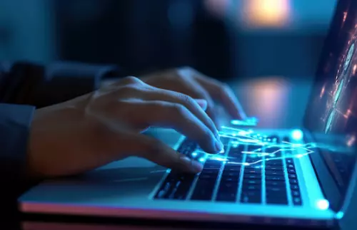 A person typing with illuminated strokes across their laptop keyboard 